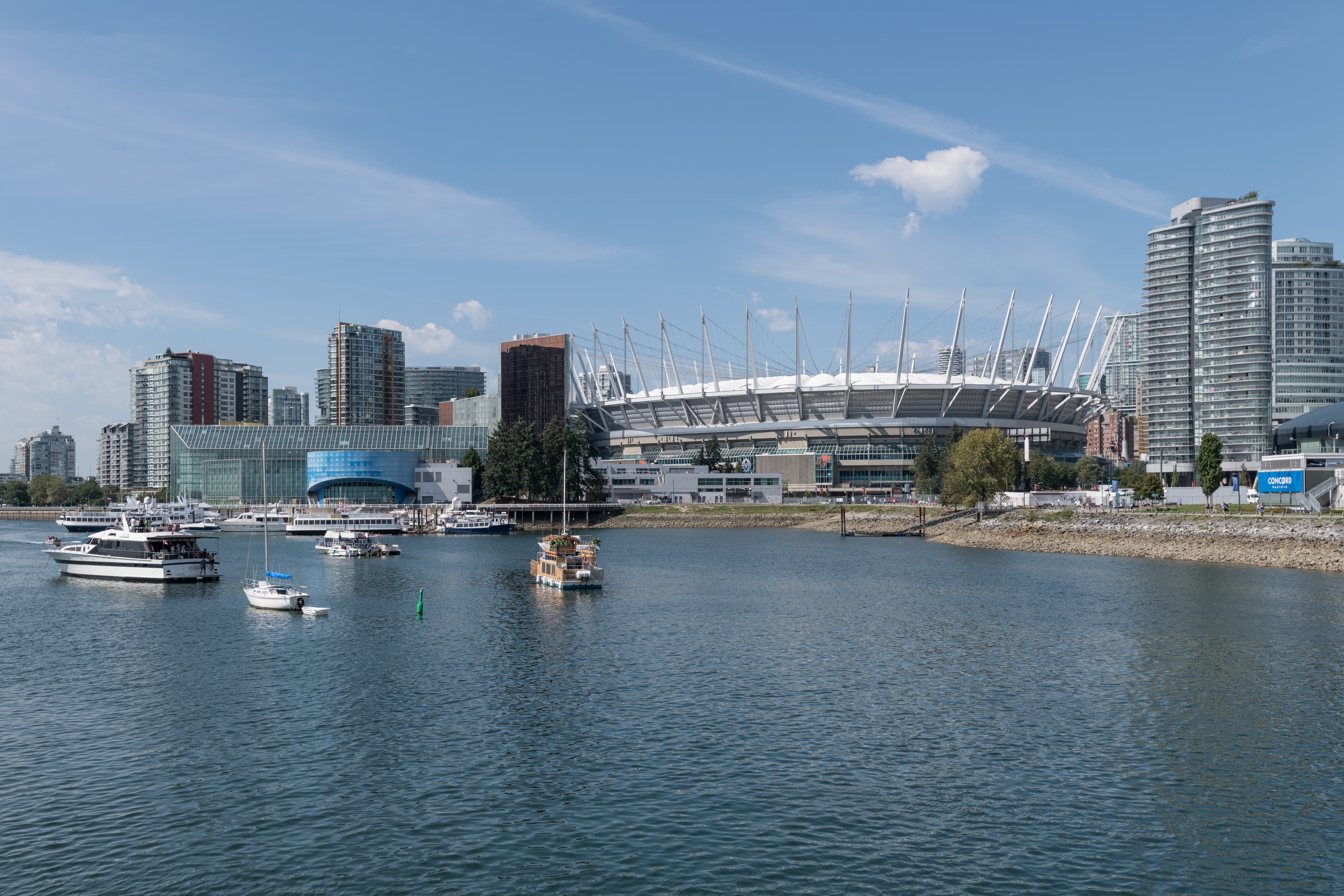 Daytime east-facing view of BC Place with downtown Vancouver buildings and clouds.