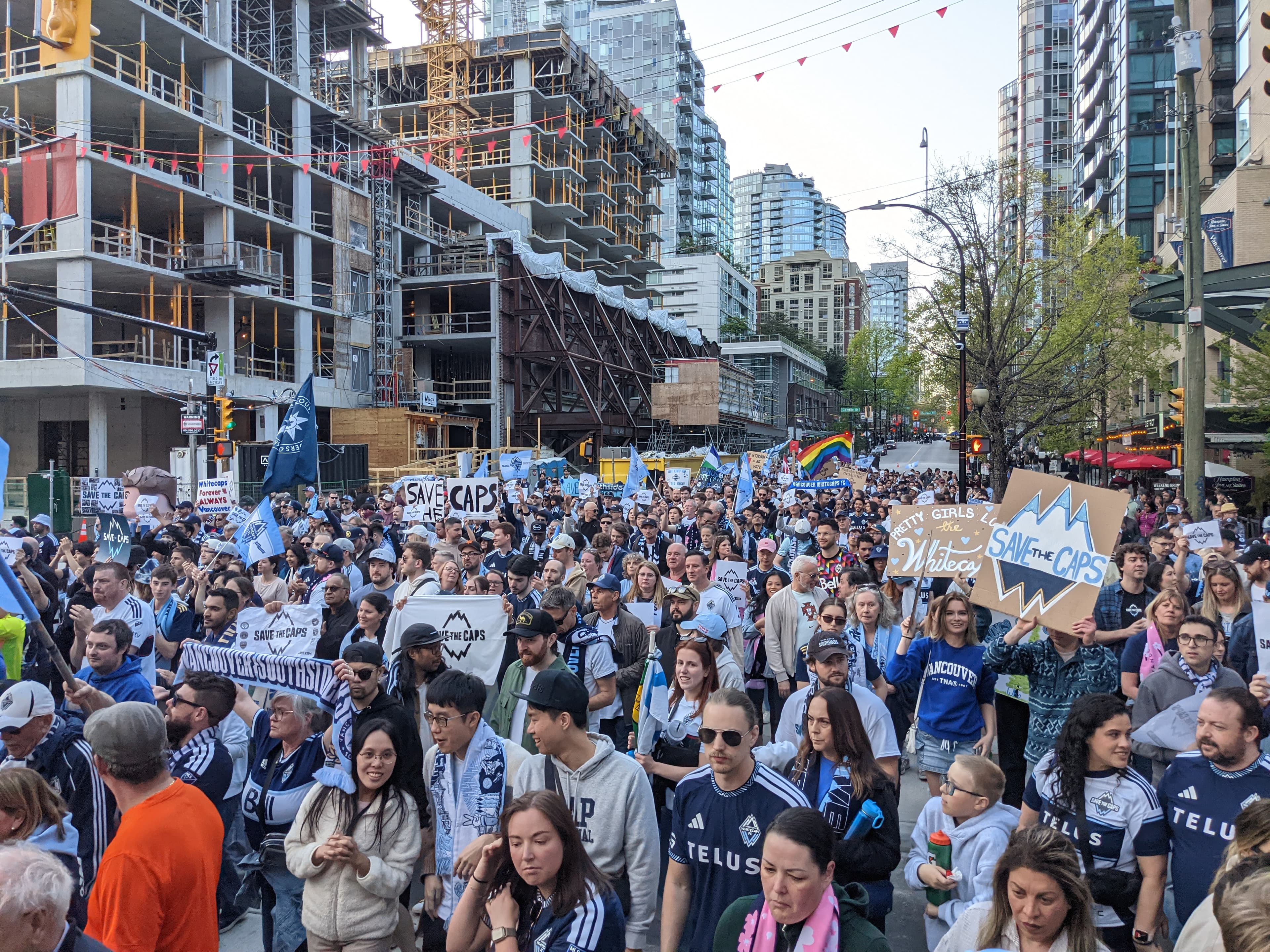 A large street march of Whitecaps supporters carries Save The Caps signs toward BC Place in downtown Vancouver.